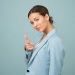 A young woman in a blue suit exhibits confidence with a relaxed pose against a blue background.